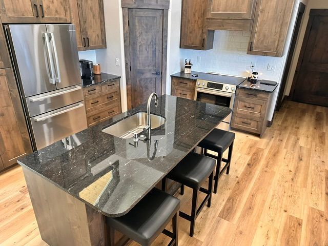 Modern kitchen with granite island, bar stools, stainless appliances, and wood floors.