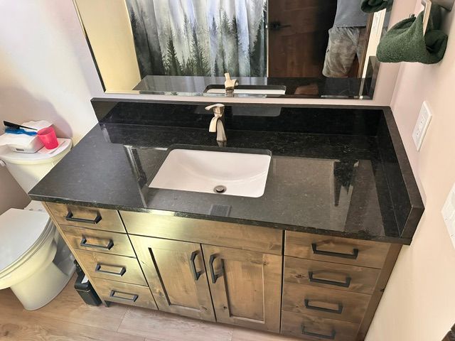 Bathroom vanity with black granite countertop, white sink, and wooden cabinets beneath a mirror