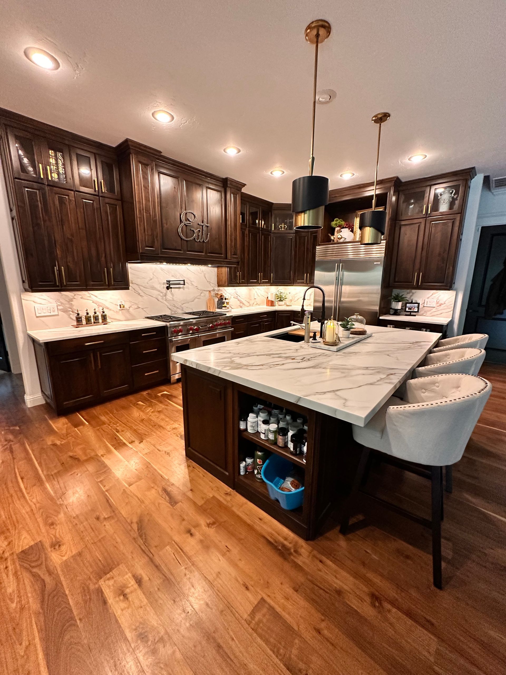 Modern kitchen with dark wood cabinets, white marble island, pendant lights, and hardwood floors