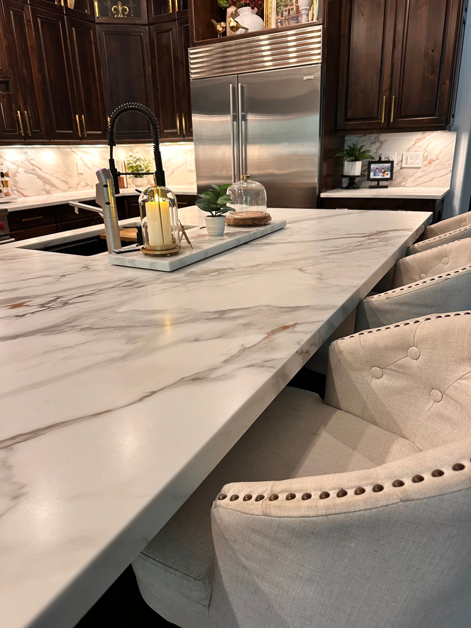 Modern kitchen with marble island, bar stools, stainless steel fridge, and dark wood cabinets