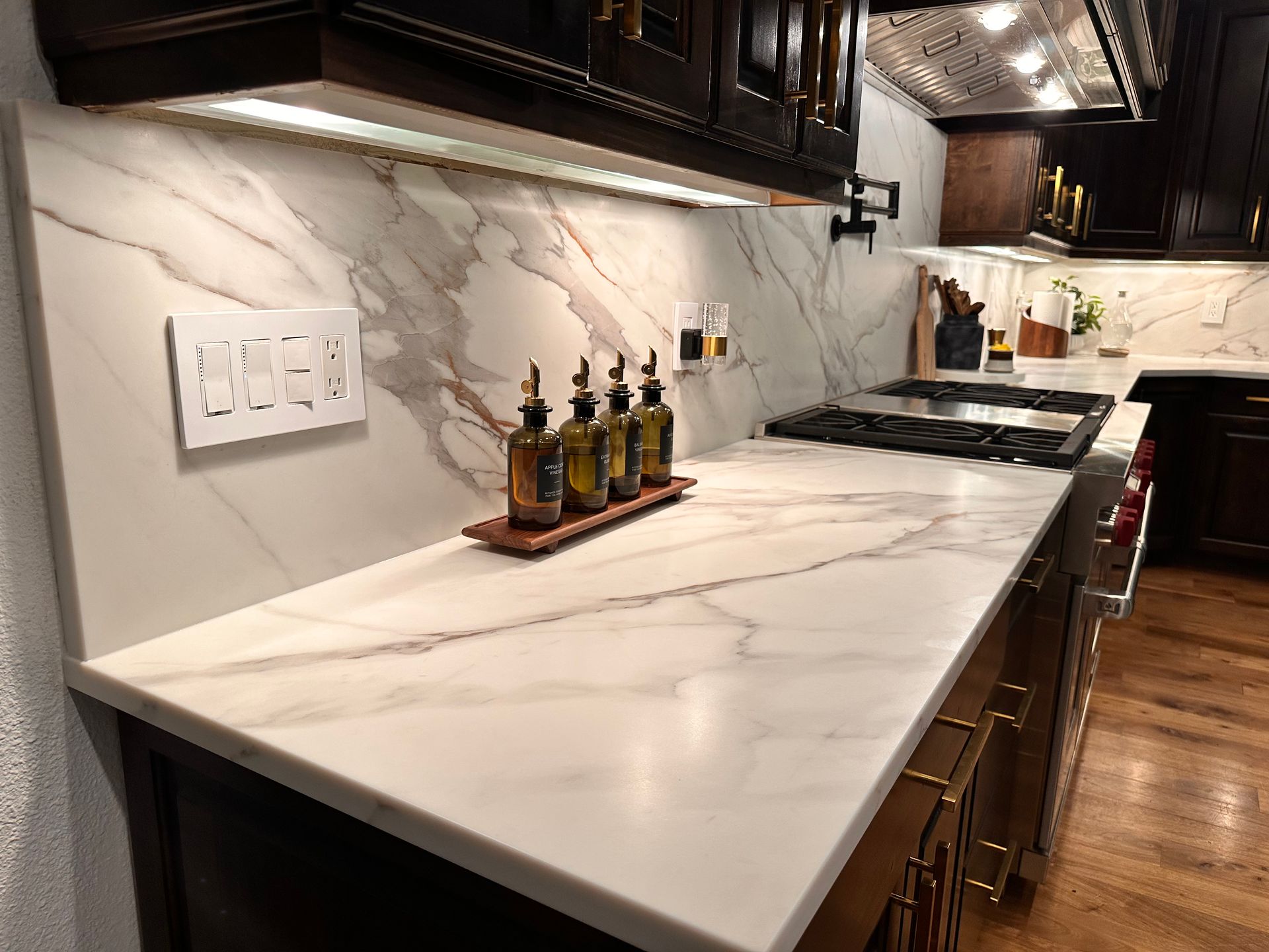 Modern kitchen with white marble countertop, dark cabinets, and bottles of olive oil near a stovetop