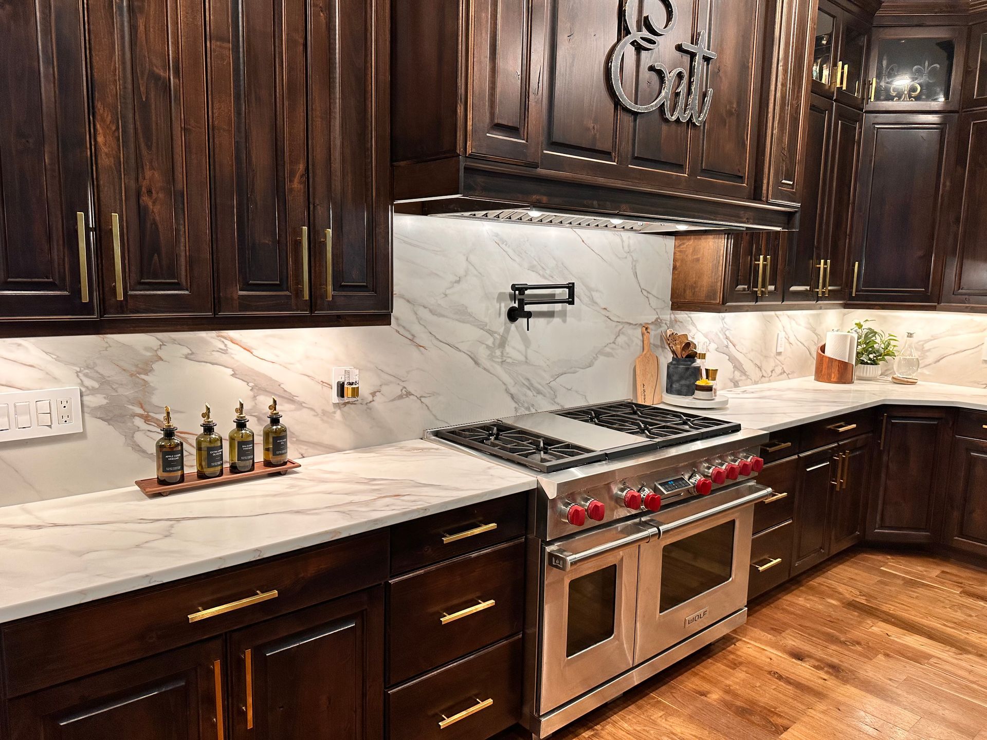 Dark wood kitchen with marble countertops, stainless steel stove, and white backsplash