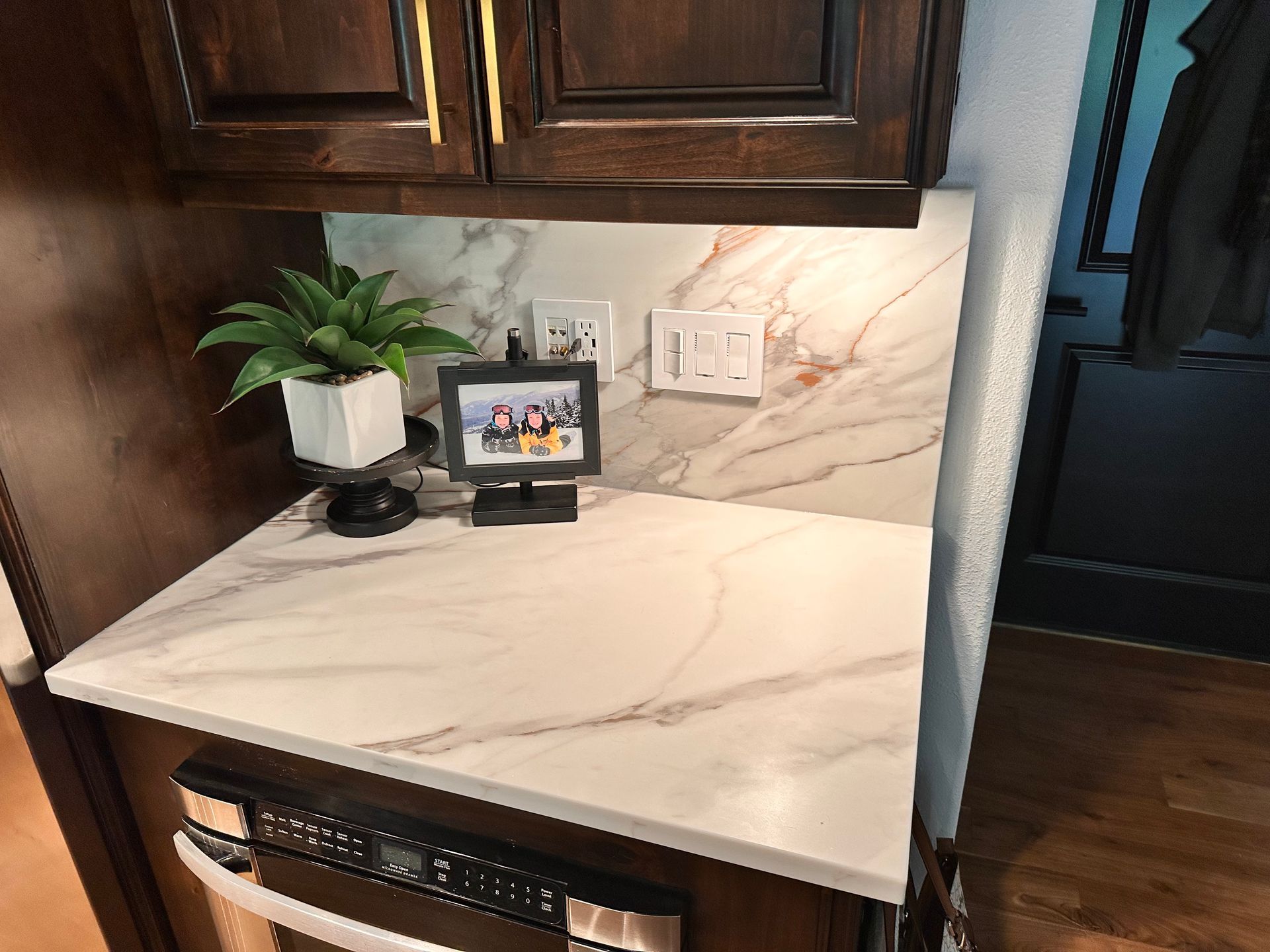 Kitchen counter with white marble top, small plant, tablet on stand, and built-in wine cooler below.