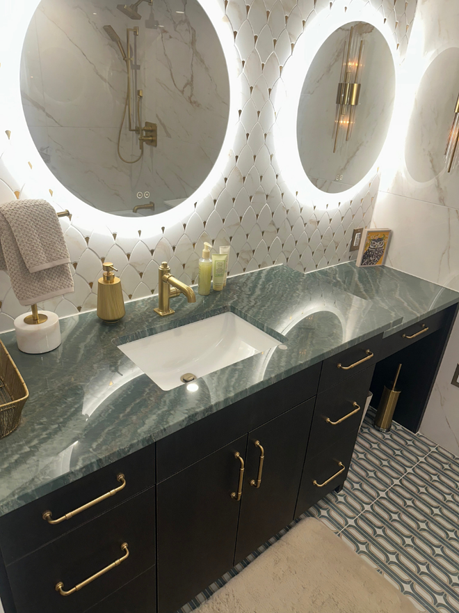 Elegant bathroom vanity with round LED mirrors, marble countertop, black cabinets, and gold fixtures
