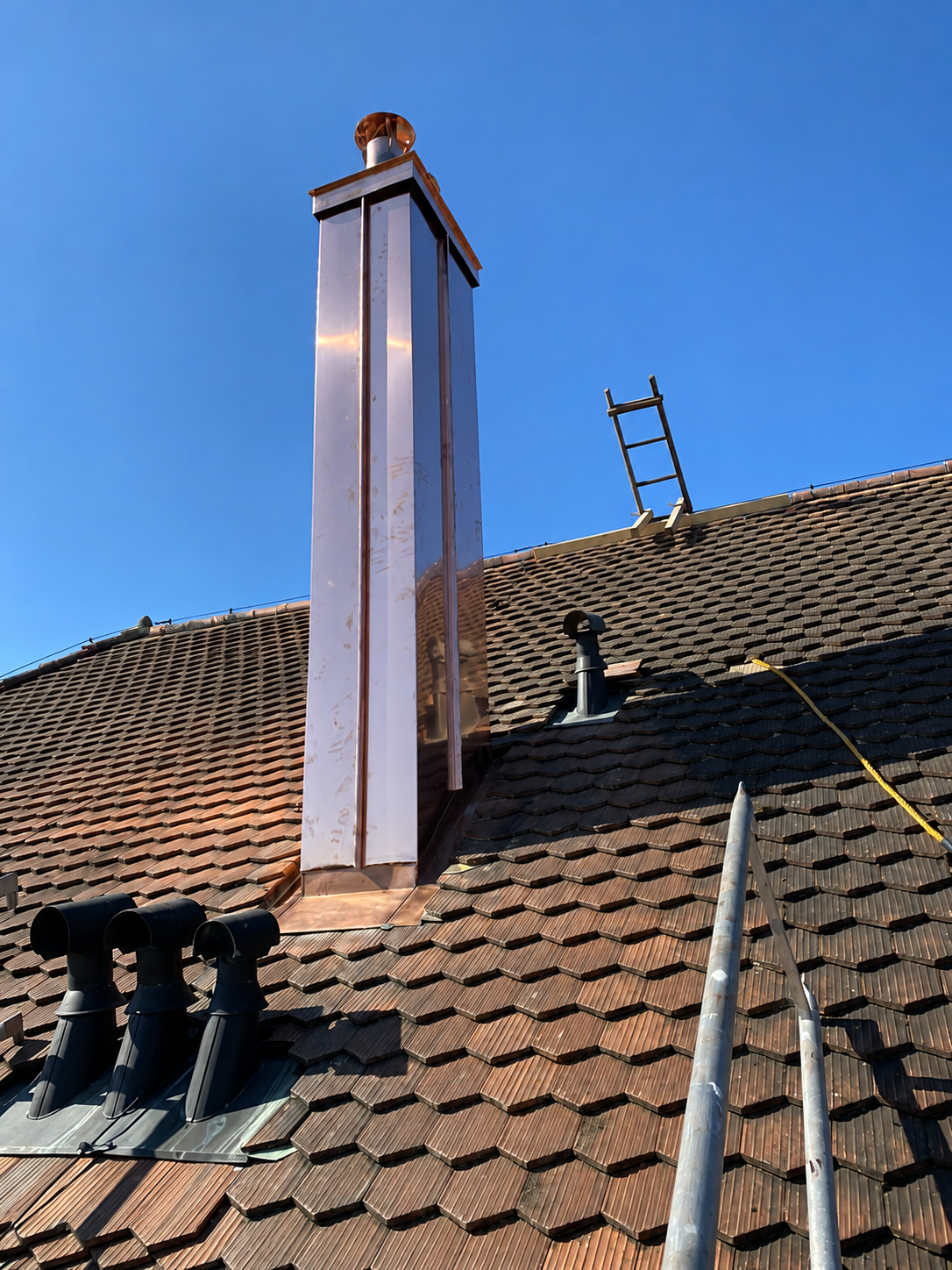 Cheminée de couvreur avec échafaudage sur un toit de tuiles, se détachant sur un ciel bleu.