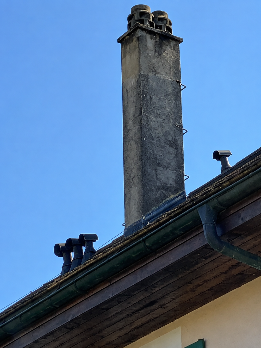 Toiture avec une haute cheminée grise se détachant sur un ciel bleu clair