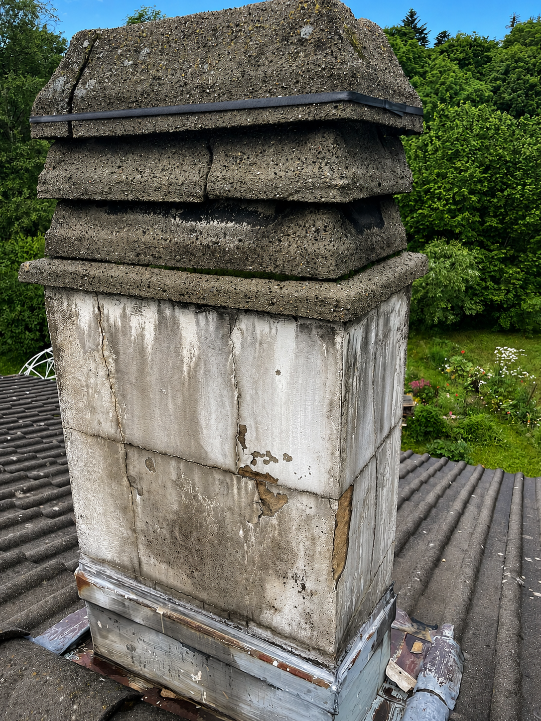 Cheminée en pierre patinée, coiffée d'un toit de chaume, sur un toit entouré de verdure.