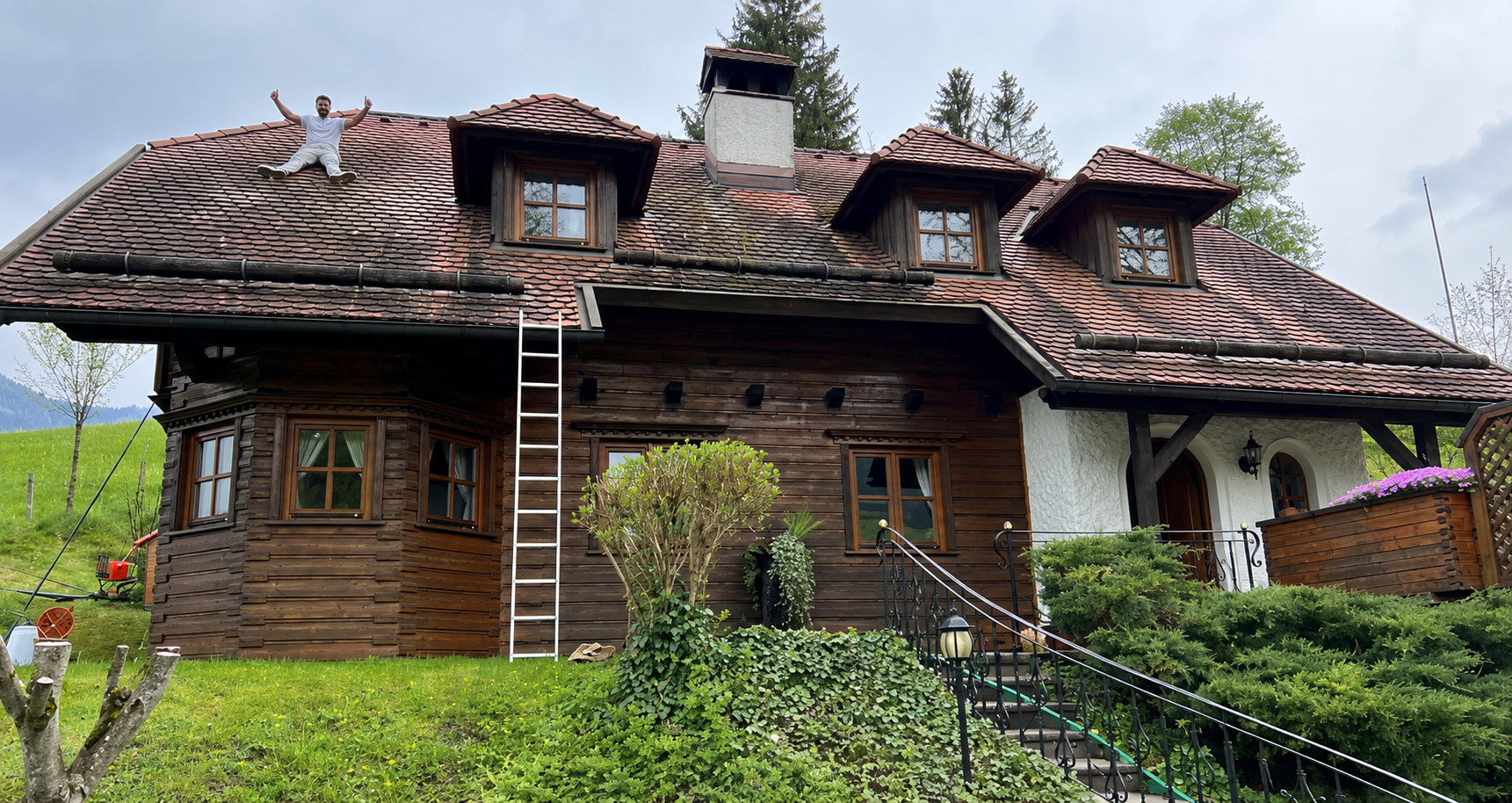 Maison rustique en bois avec un toit de tuiles, des lucarnes et une échelle appuyée contre la façade.