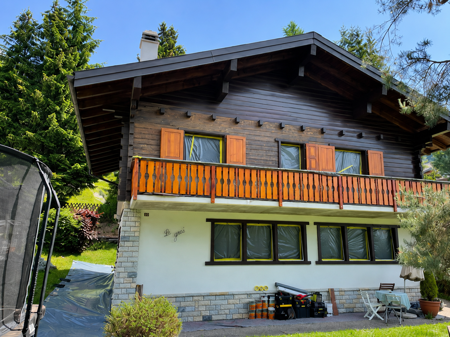 Maison de style chalet avec balcon en bois, murs inférieurs blancs et chemin de pierre dans un cadre verdoyant.