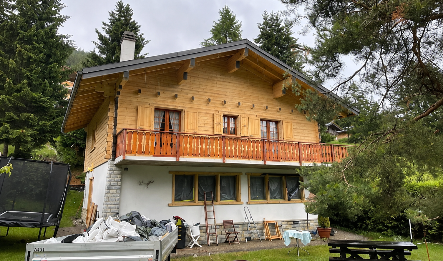 Maison de style chalet en bois avec balcon orange dans une cour boisée, avec vélos et mobilier de jardin