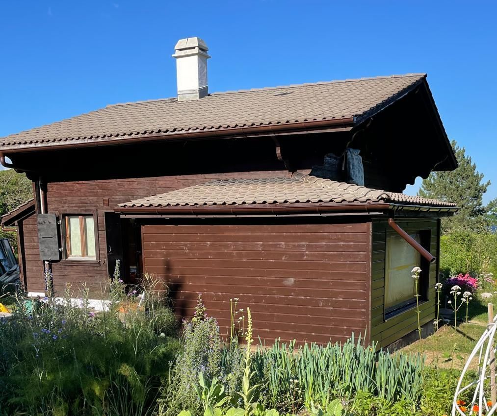 Maison brune à deux étages avec garage, toit beige et jardin à l'avant sous un ciel bleu