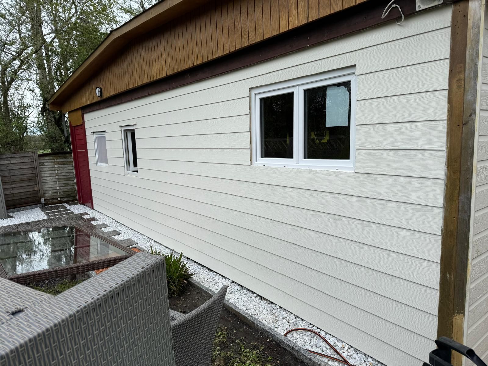 Façade d'un bâtiment blanc avec fenêtres, boiseries et patio humide au premier plan