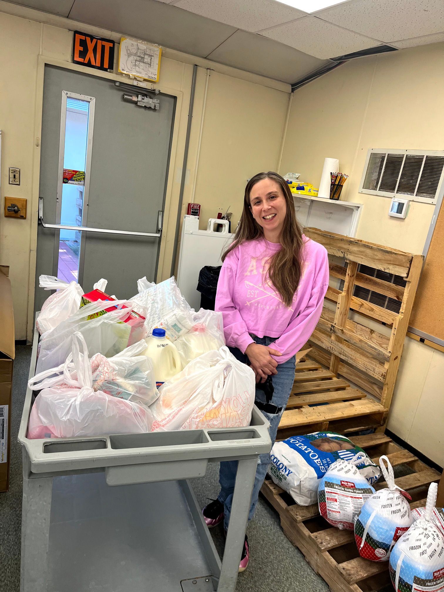 Woman in a pink sweater standing beside a cart of bagged donations in a storage room