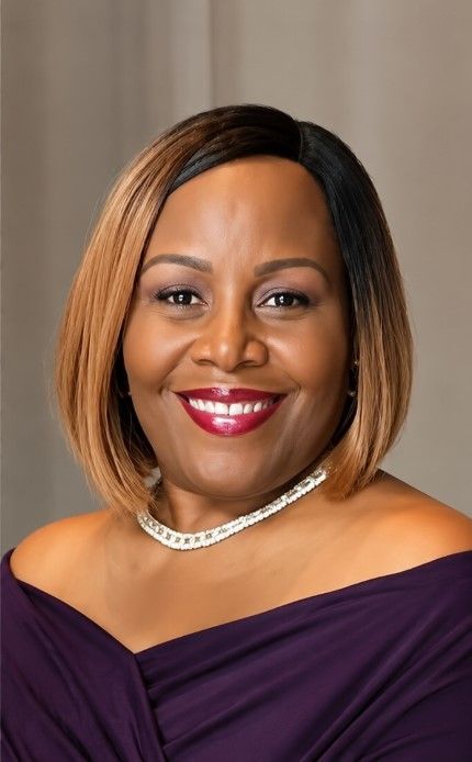 Smiling woman in a red blouse and silver necklace, standing indoors against a warm background