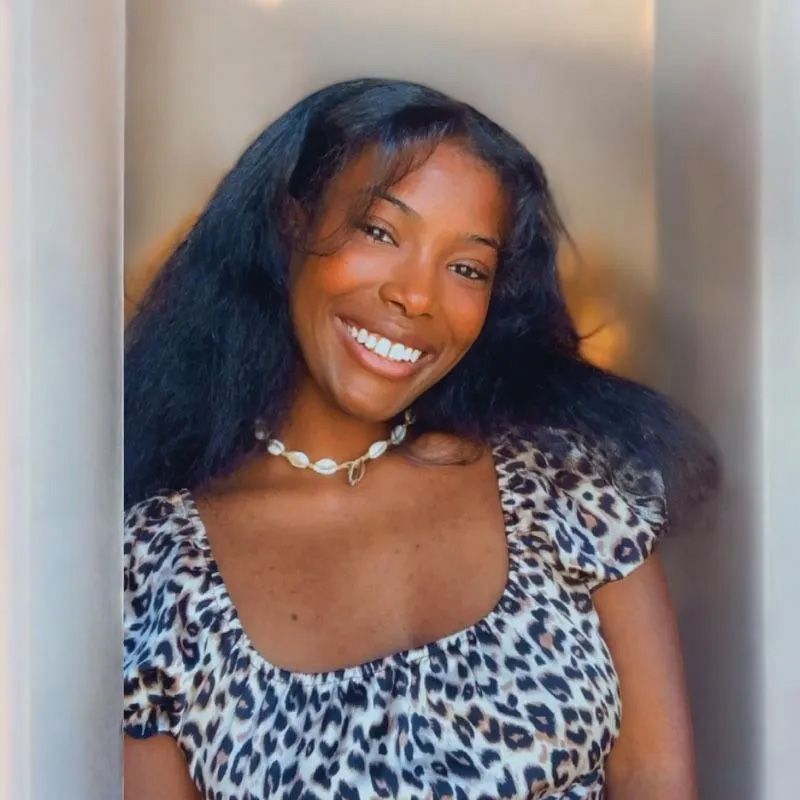 Smiling woman in a leopard-print top and pearl necklace posing indoors with warm light