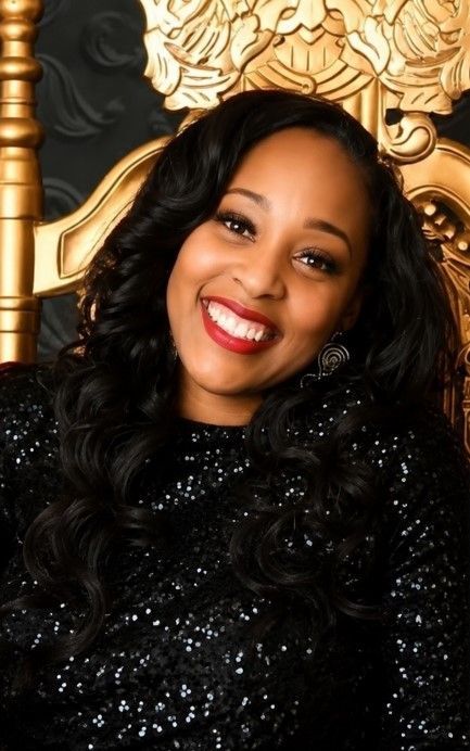 Smiling woman in a leopard-print top and pearl necklace posing indoors with warm light
