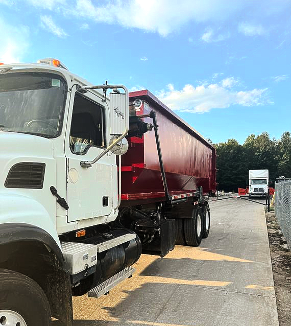 White cab dump truck with red trailer parked on a paved lot under a blue sky