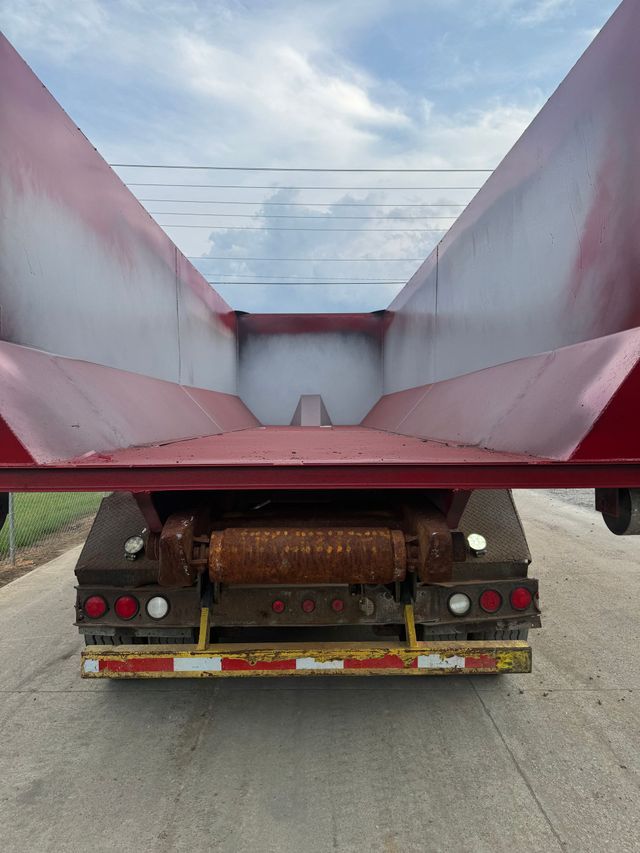 Rear view of a truck carrying a large red metal dump bed or hopper on a road.