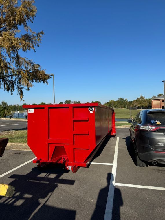 Bright red dumpster parked in a parking lot beside a black SUV under a clear blue sky