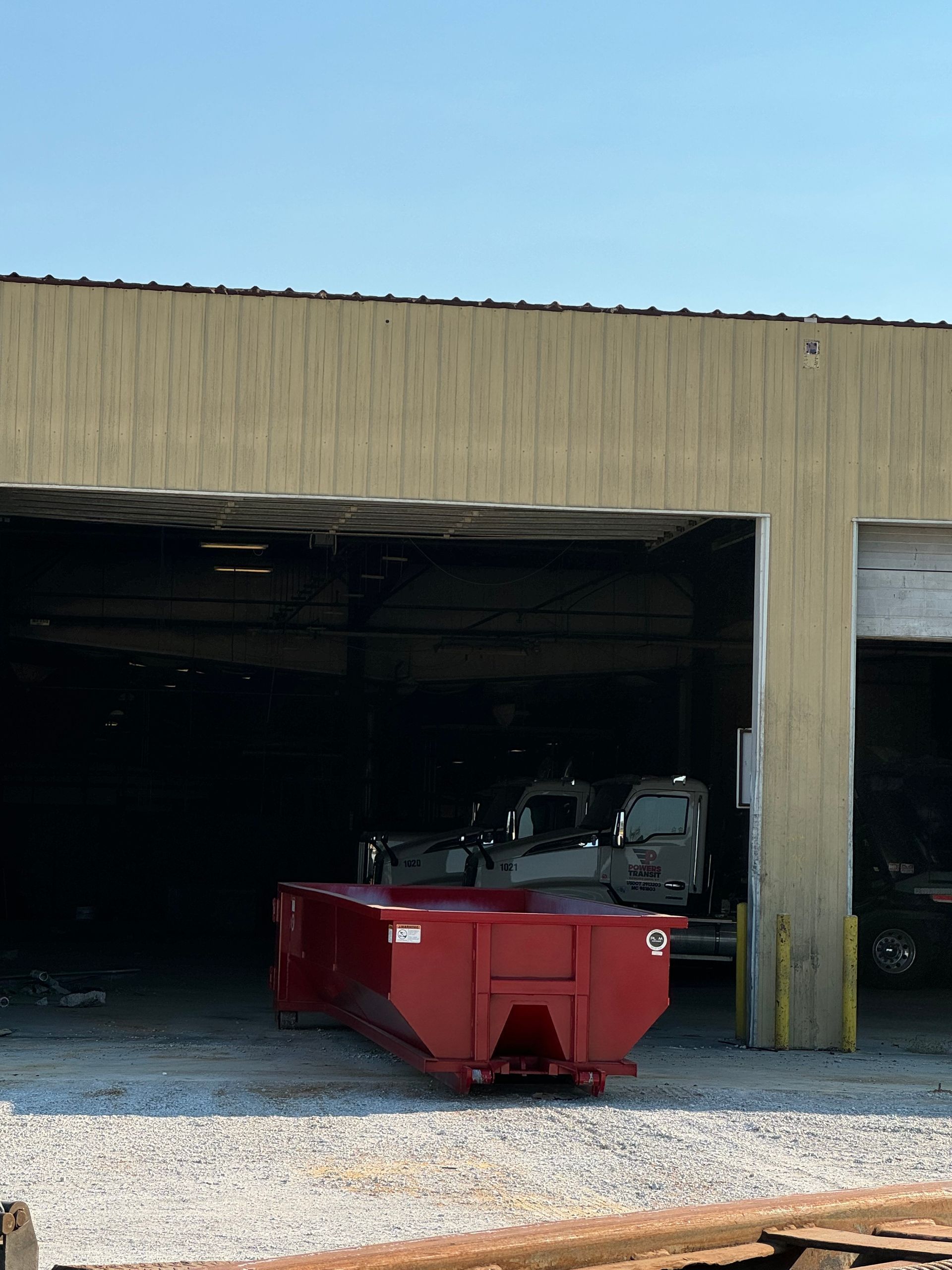 Red dumpster parked in a gravel garage bay with a dark interior.