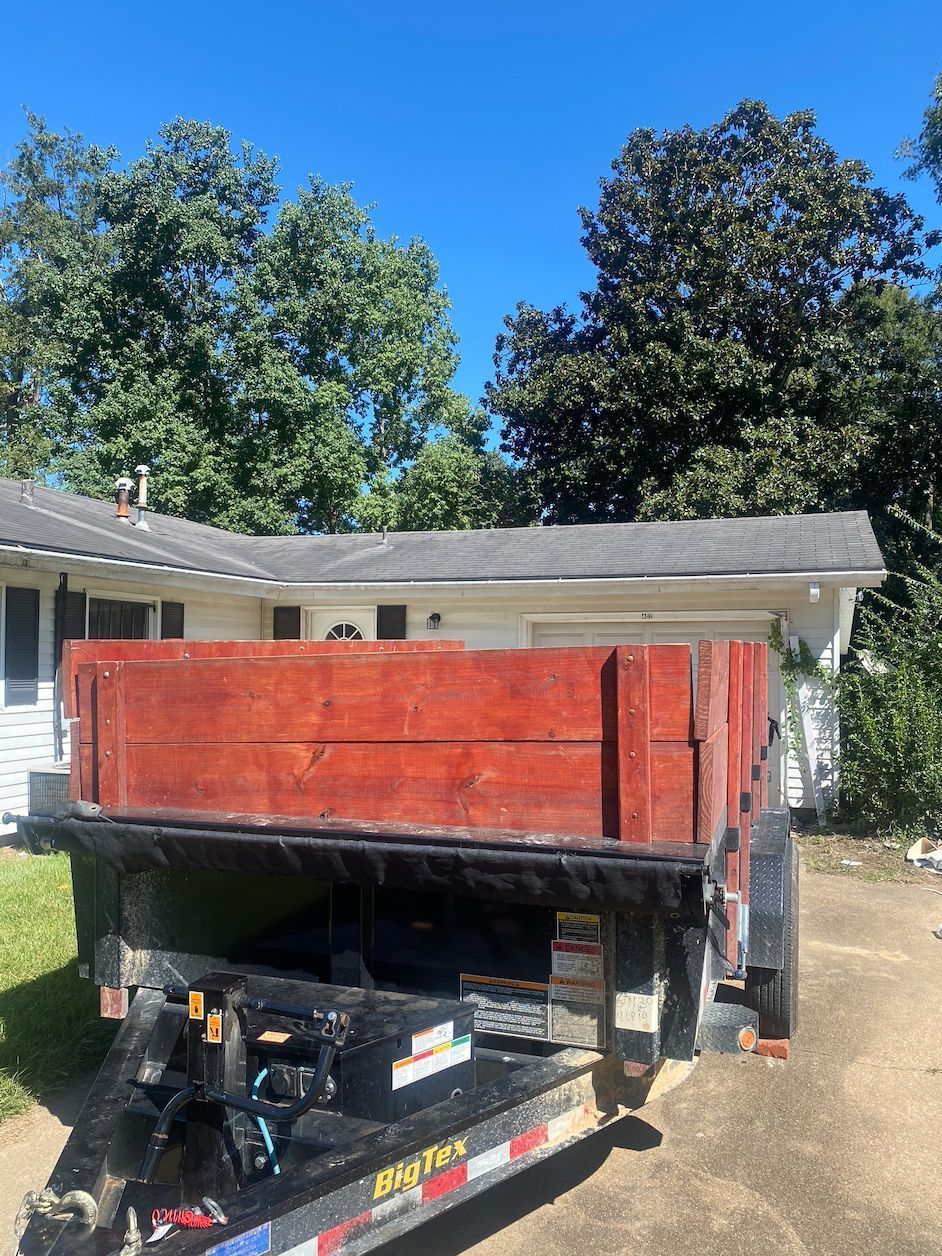 Red dump trailer with wooden sides parked in a driveway in front of a house.