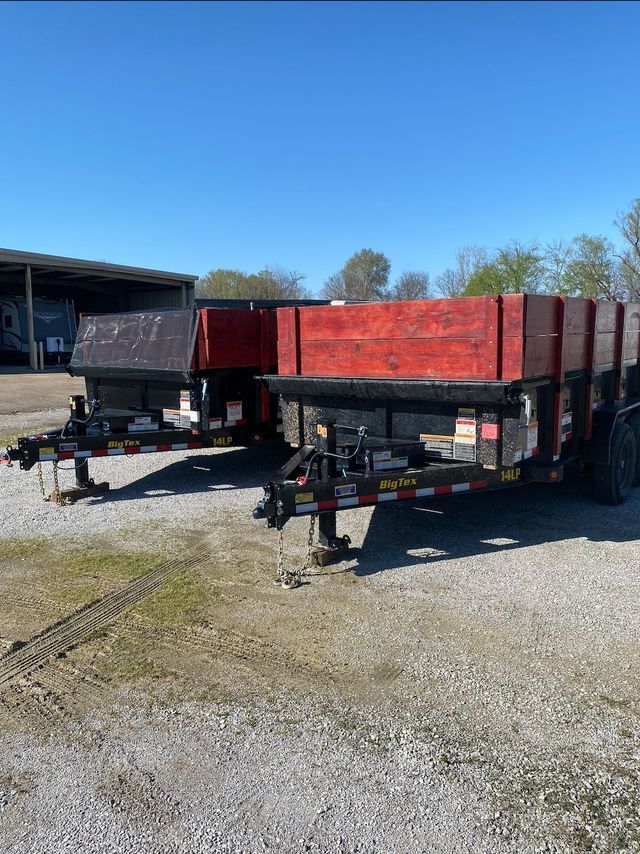Two red flatbed trailers parked on a gravel lot under a clear blue sky