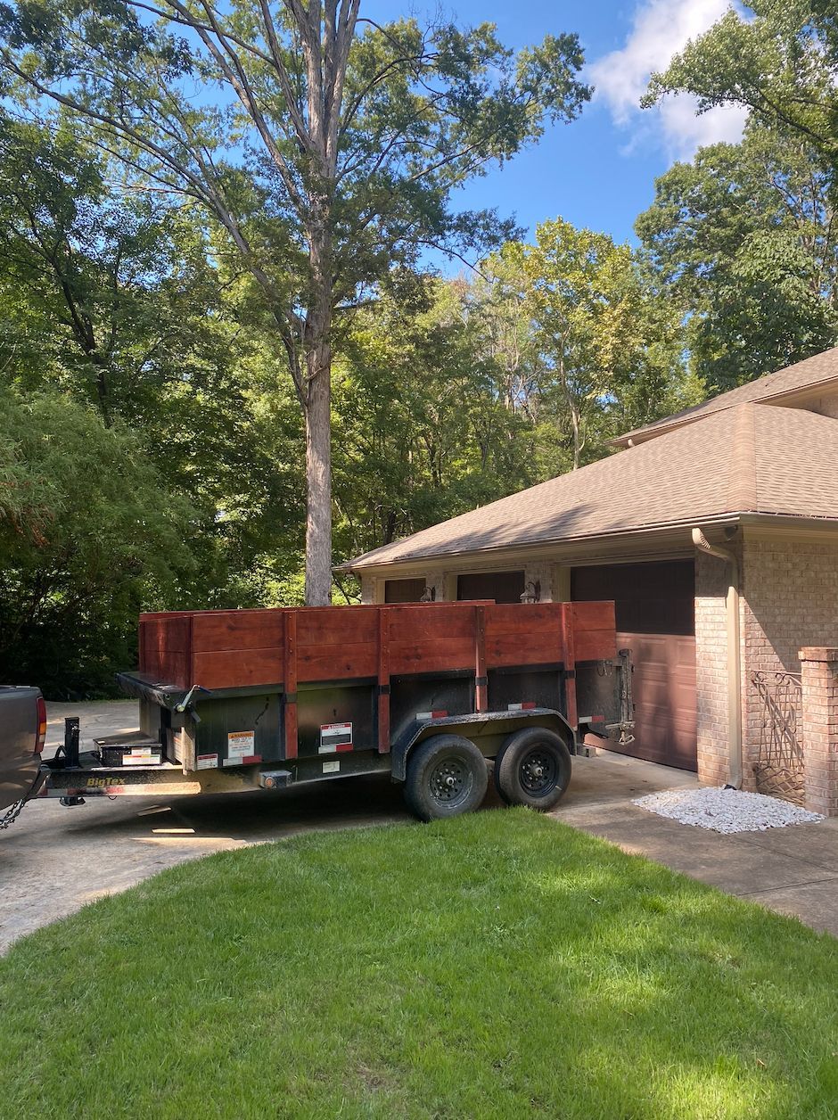 Wooden trailer parked on a driveway beside a brick house and green lawn.