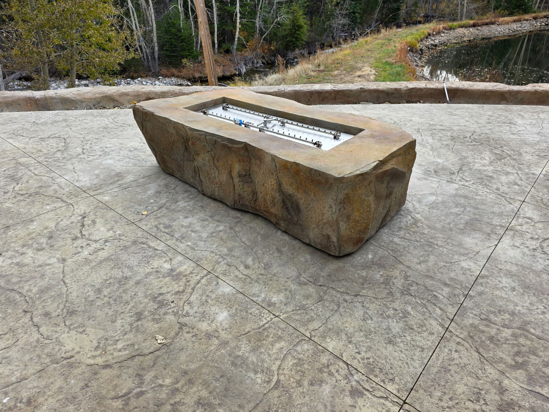 Fire burning in a dark stone bowl on a large gray rock with a rocky backdrop.