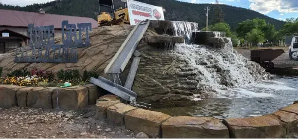 A decorative waterfall with a water sluice, surrounded by a stone border. A mountain is in the background.