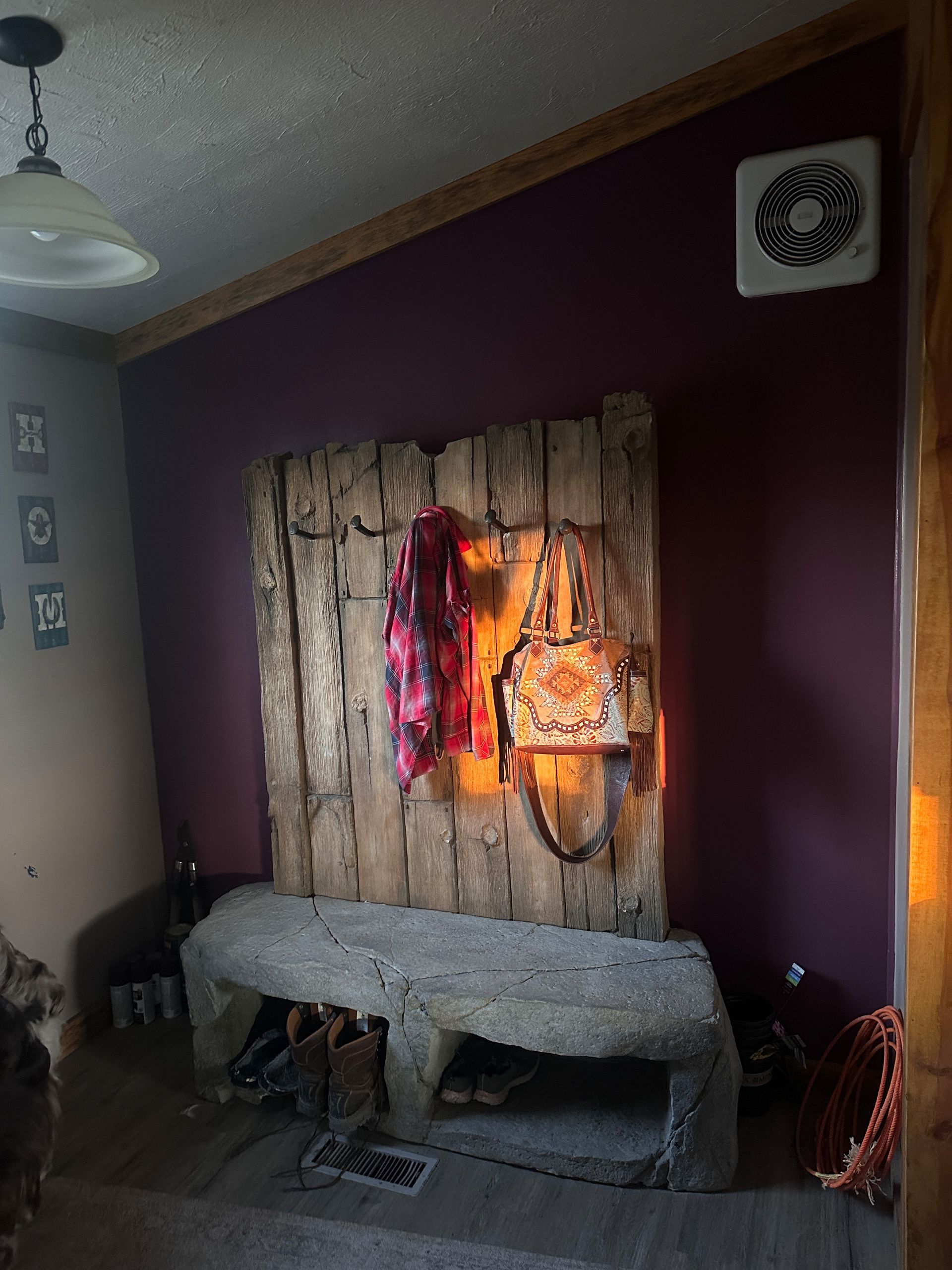 Rustic entryway with stone bench, wooden backdrop, scarf, bag, and purple wall.
