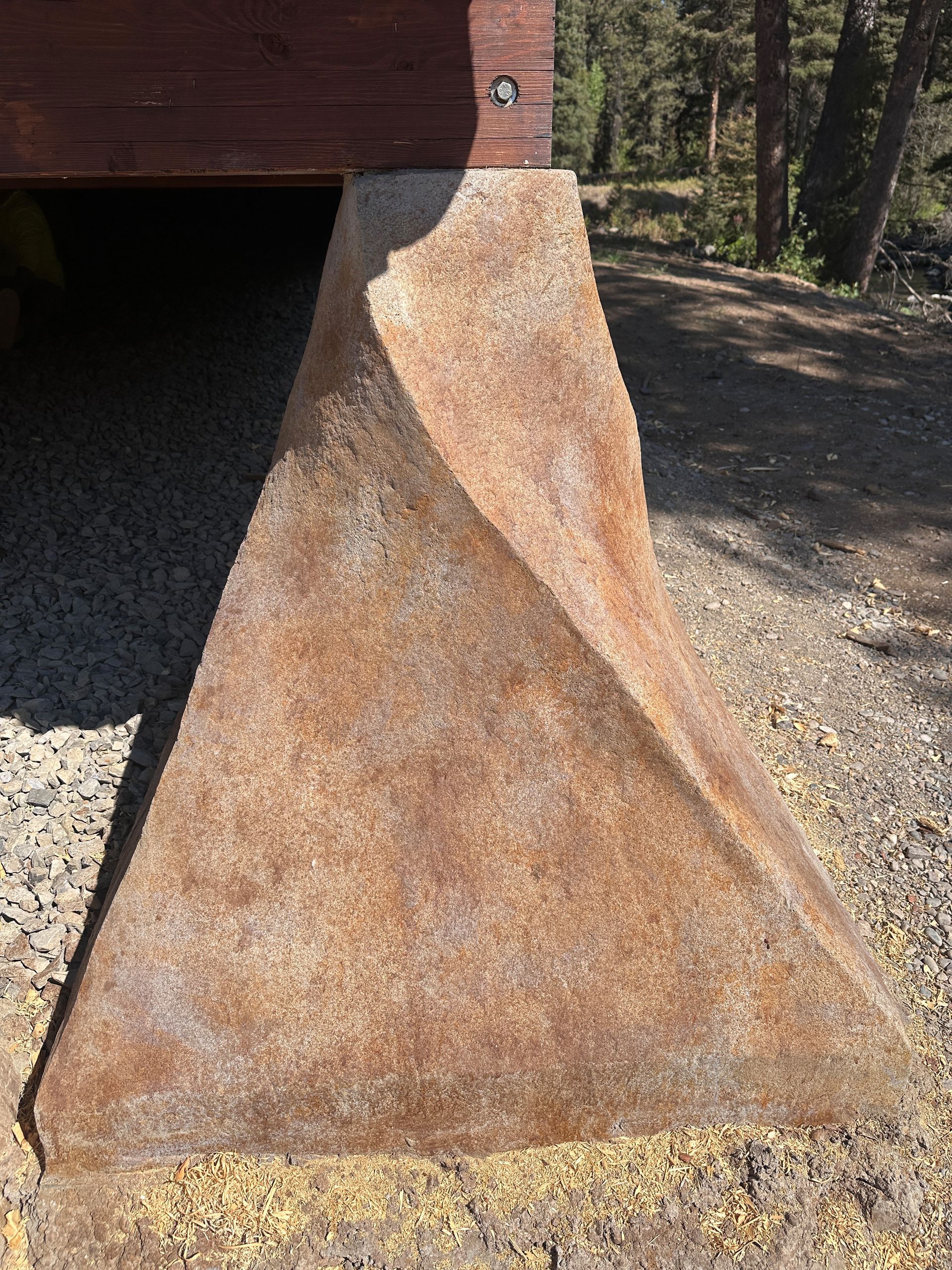 Brown triangular concrete support for a building, resting on gravel.