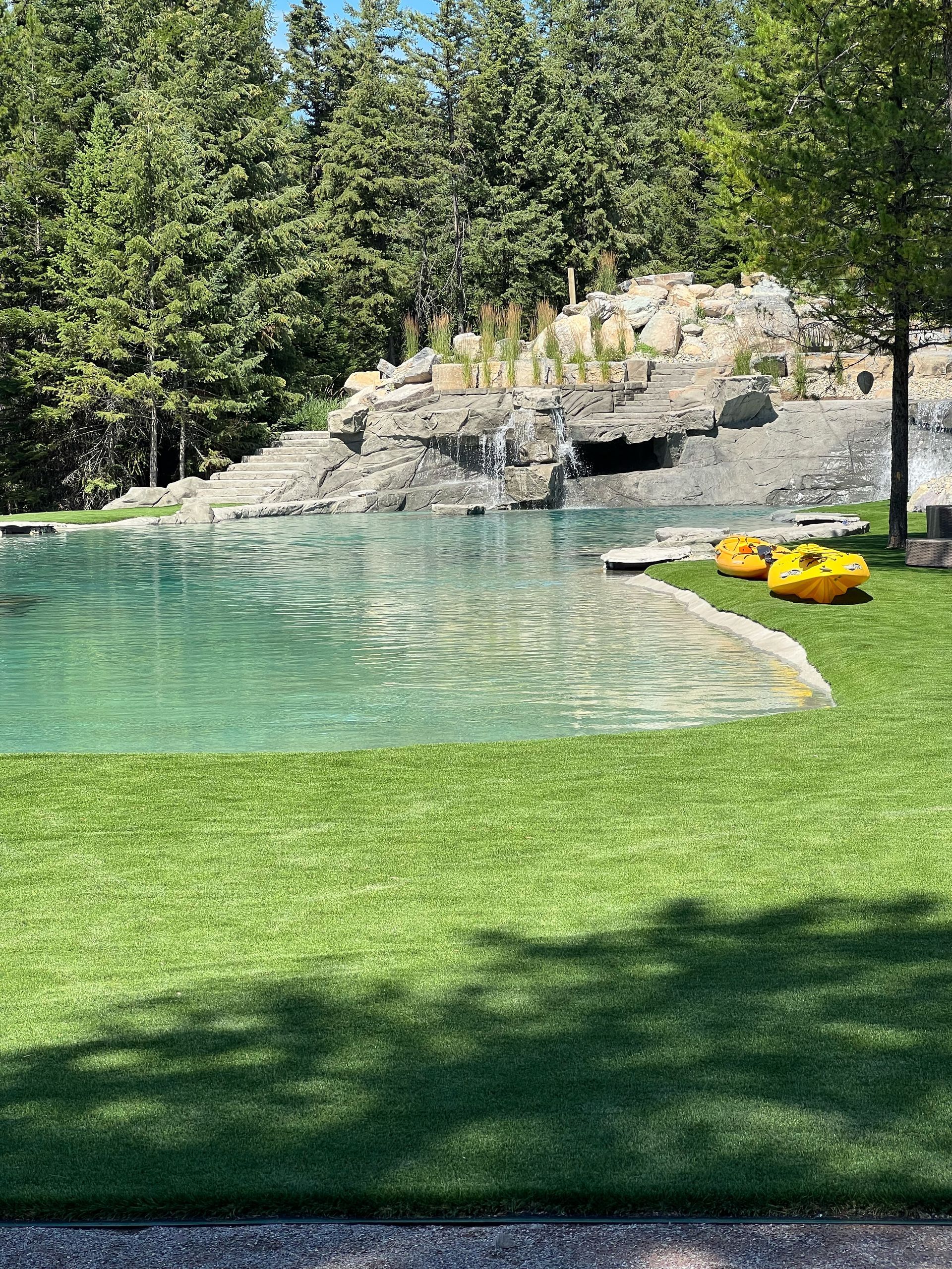 A luxury outdoor pool with a waterfall, surrounded by green grass and trees.