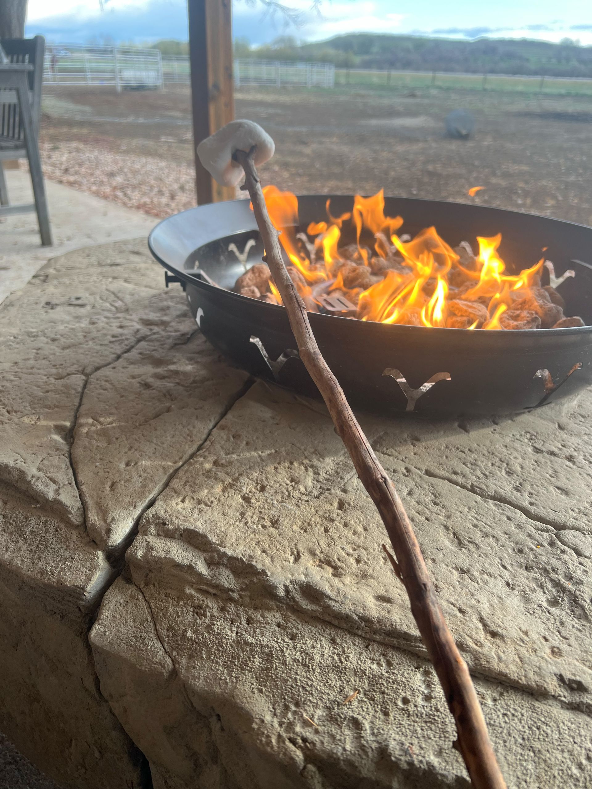 Marshmallow roasting over a fire pit on a stone patio, held on a stick.