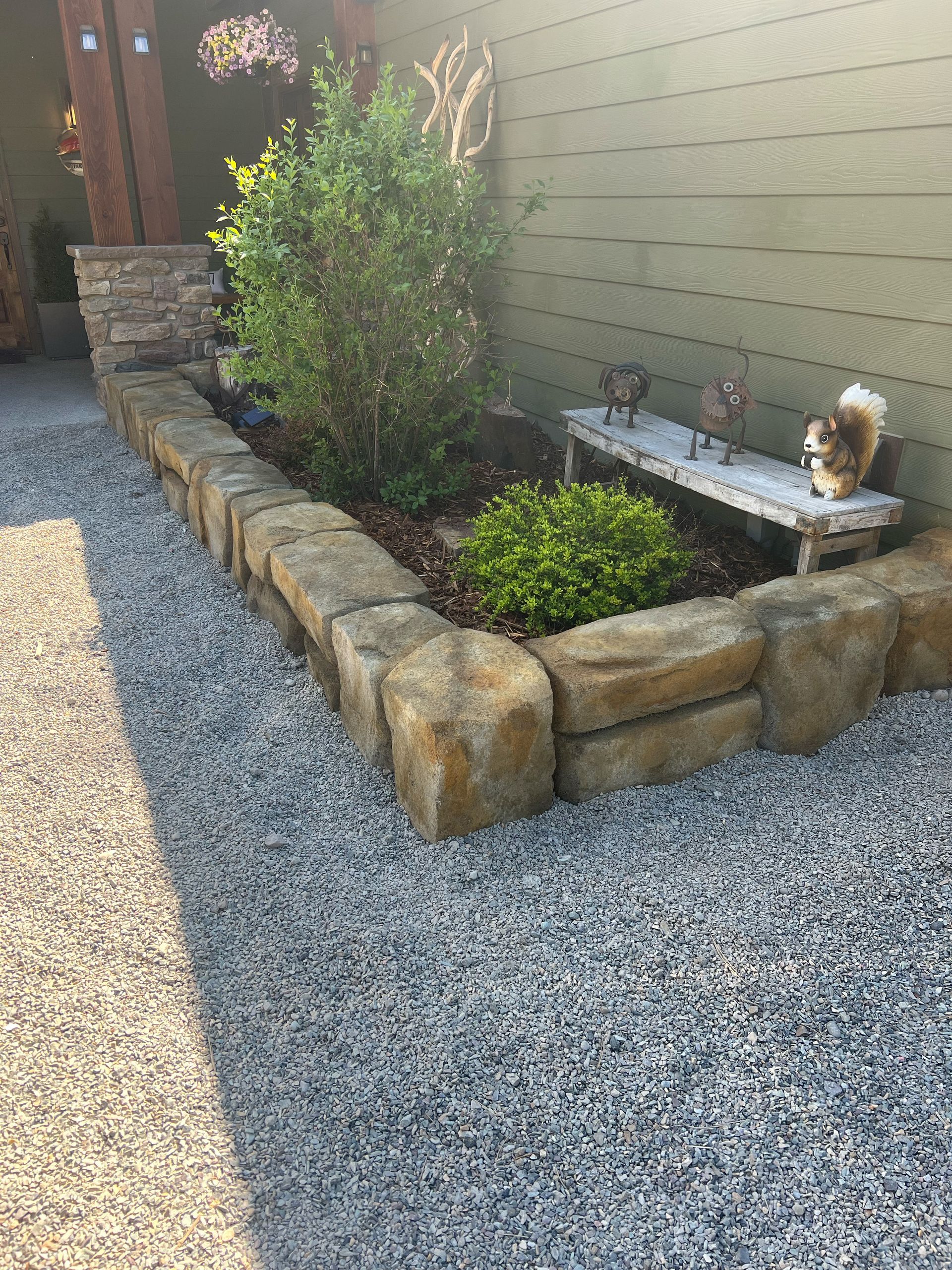 A gravel path leads to a garden bed with a stone border. A small bench with a squirrel.