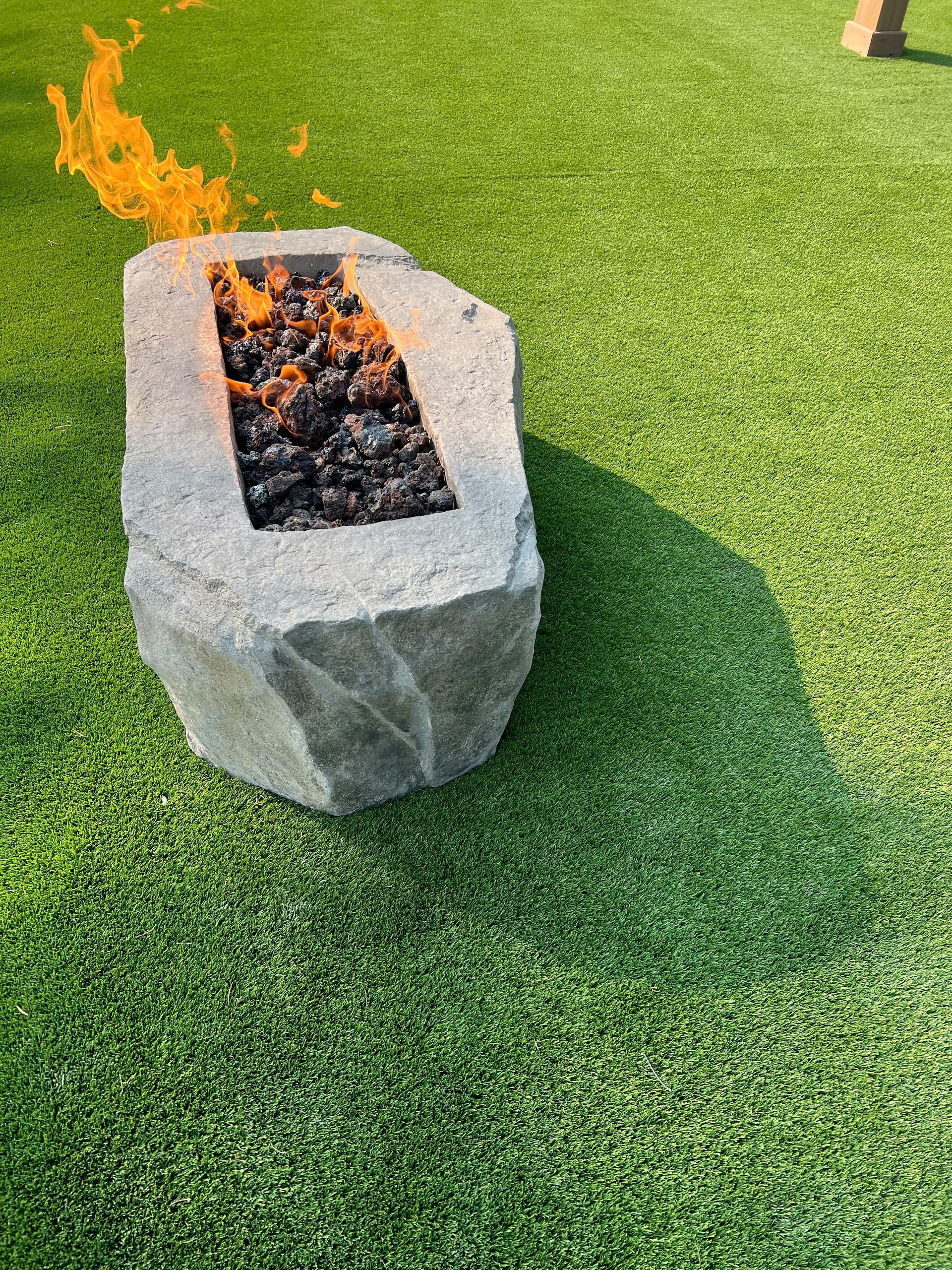 Fire pit with lit flames on a stone patio, mountain backdrop at dusk.