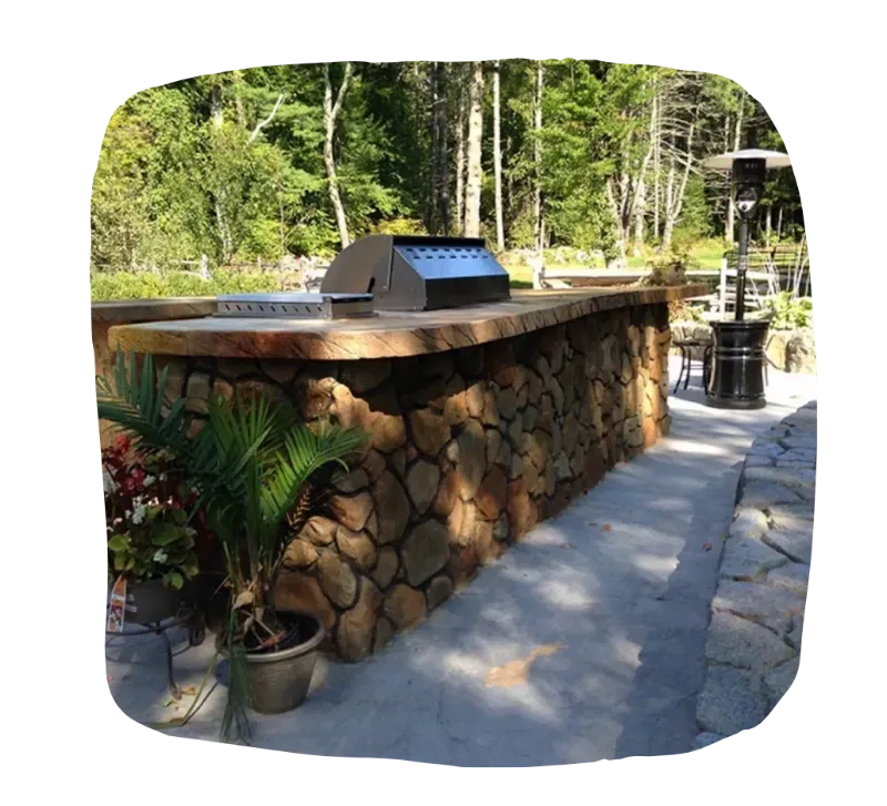 Outdoor stone grill island with stainless steel grill, potted plants, and a patio heater.