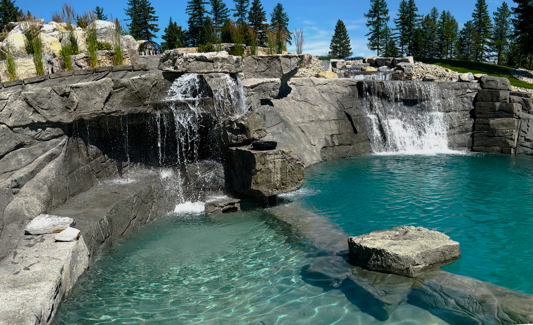 Waterfalls cascade into a turquoise pool surrounded by gray rock formations.