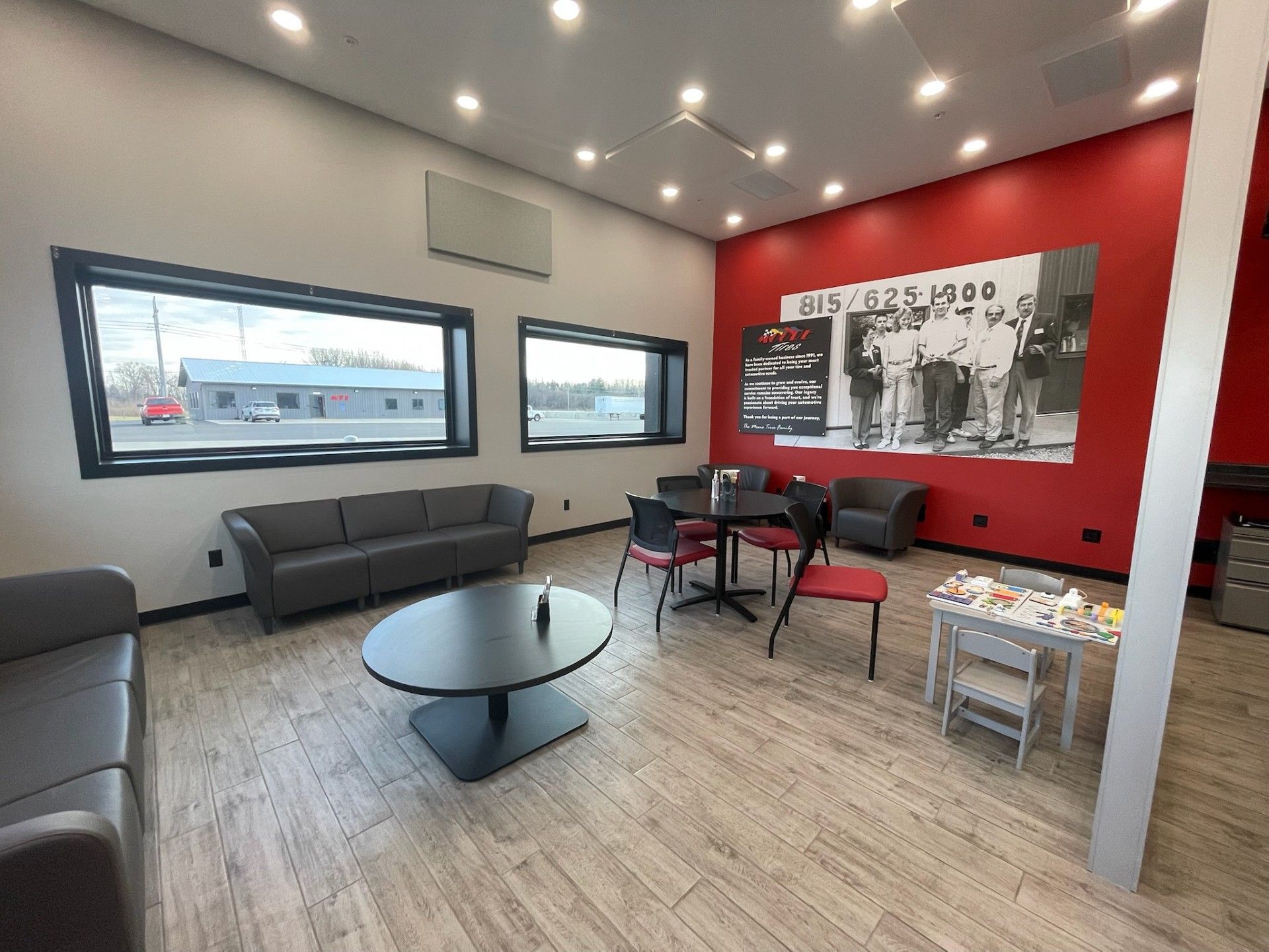 Interior of waiting area with red wall, seating, round table, and a black and white photo.