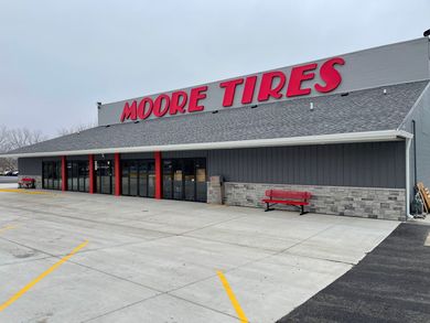 Moore Tires storefront with red sign, gray building, and parking lot.