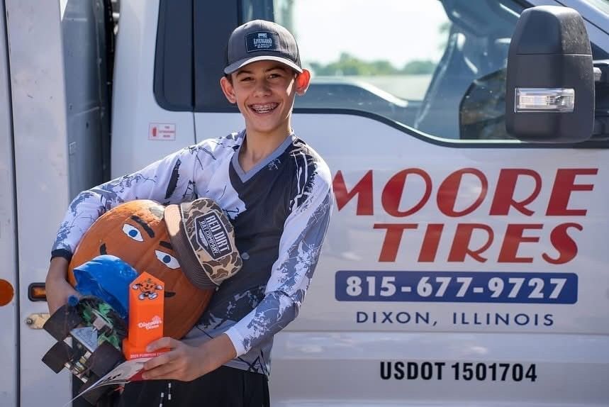 Boy with braces smiles, holding prizes in front of a Moore Tires truck in Dixon, Illinois.