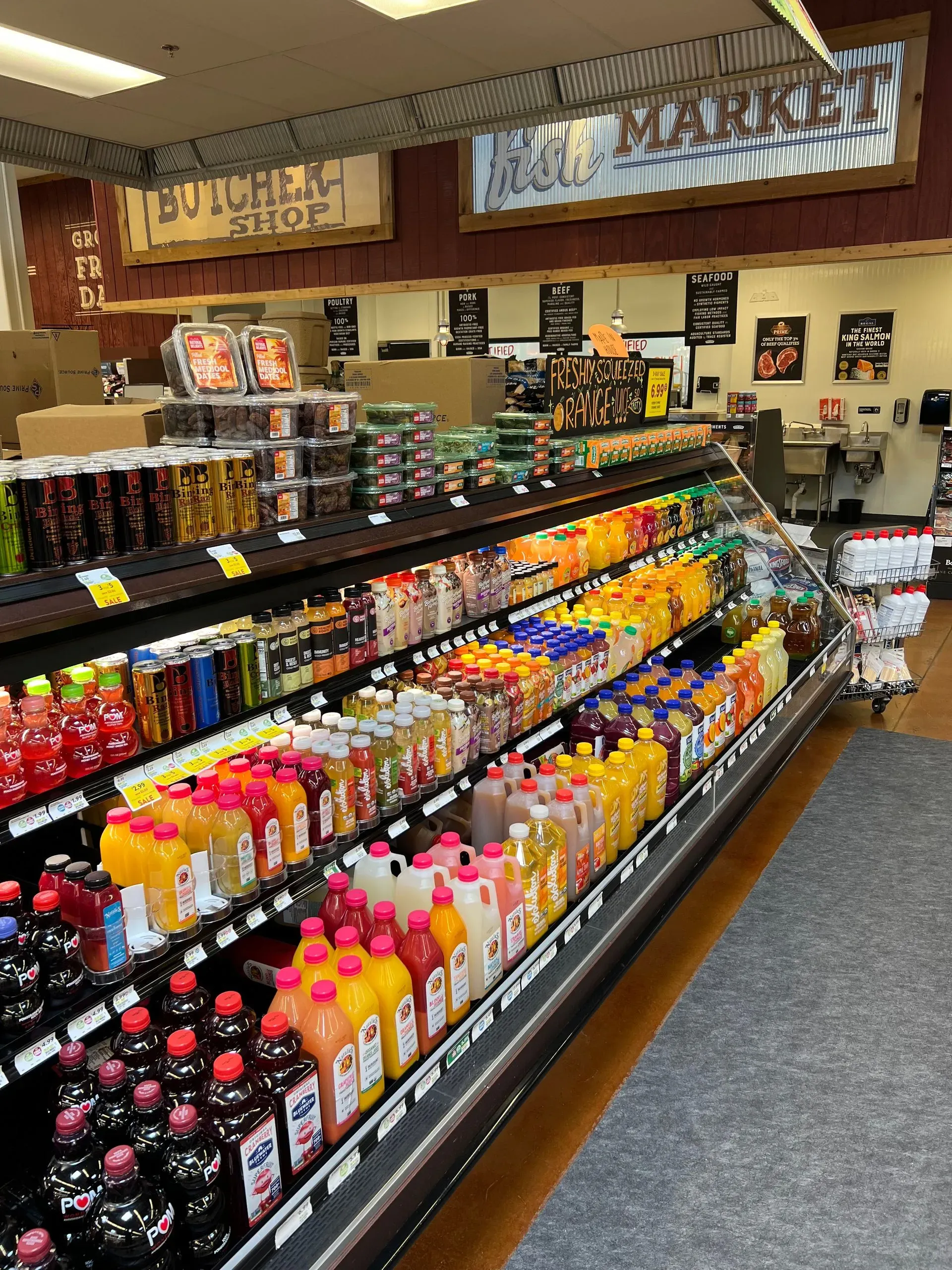 A refrigerated aisle in a grocery store stocked with rows of colorful juices and drinks. 