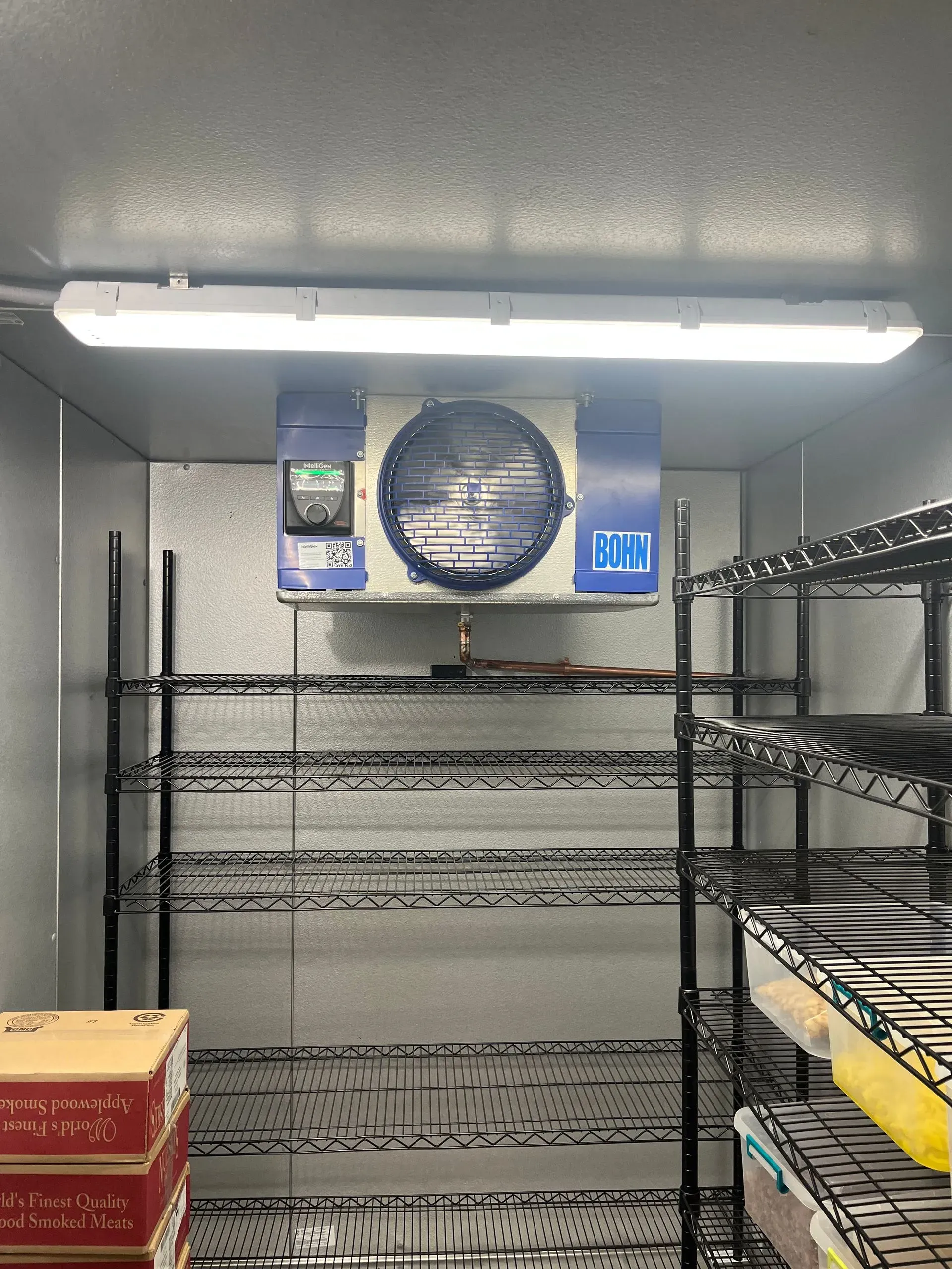 Walk-in refrigerator with shelving and a large cooling unit.