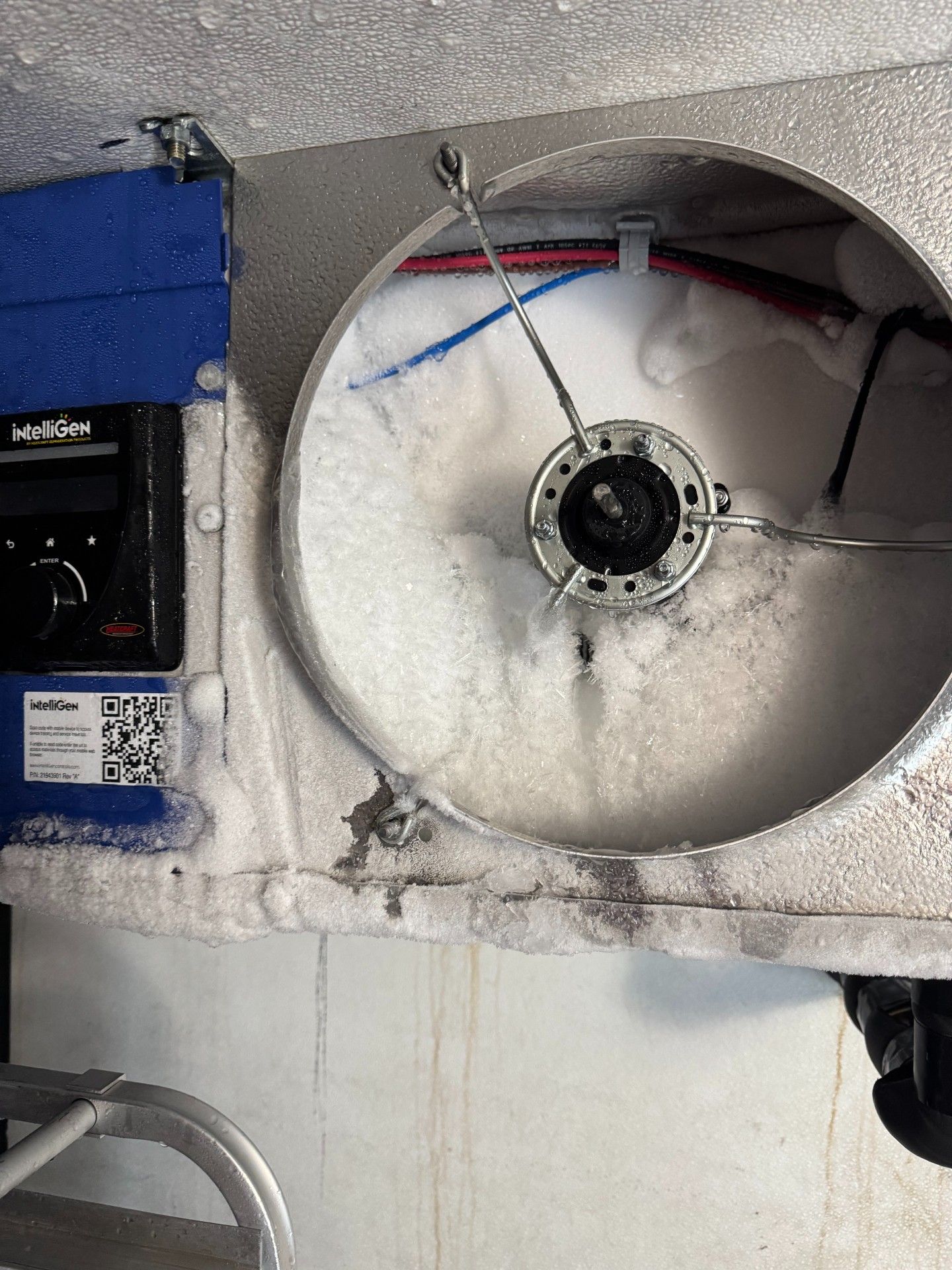 Circular fan in a freezer-like compartment, covered in ice. Wires and electrical components visible.