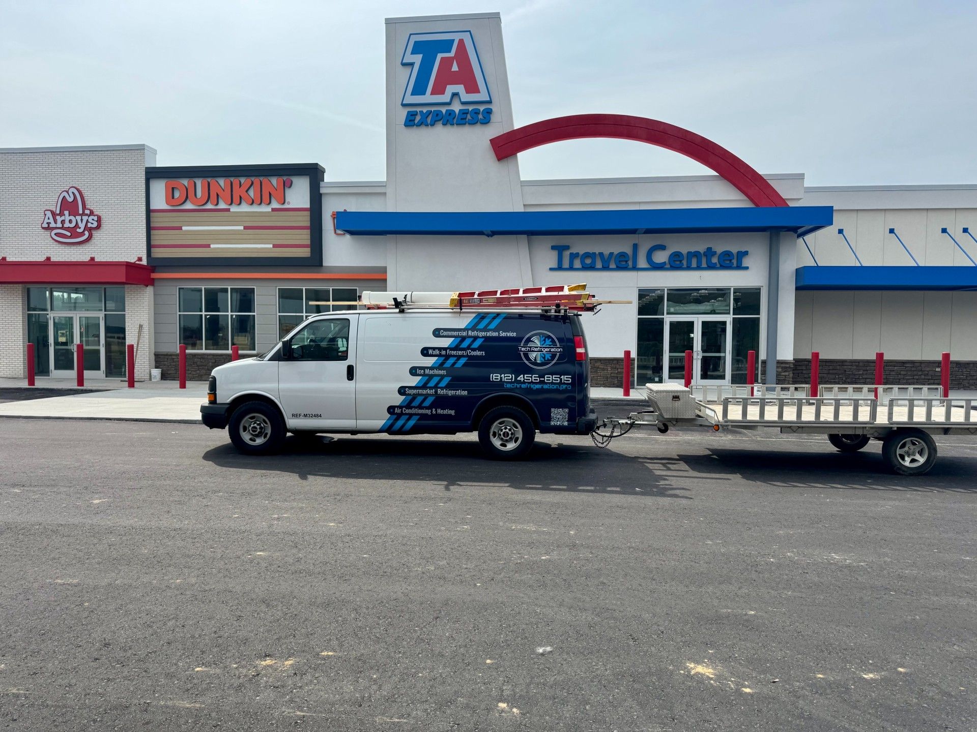 White van with trailer parked at TA Express travel center next to a Dunkin' Donuts.