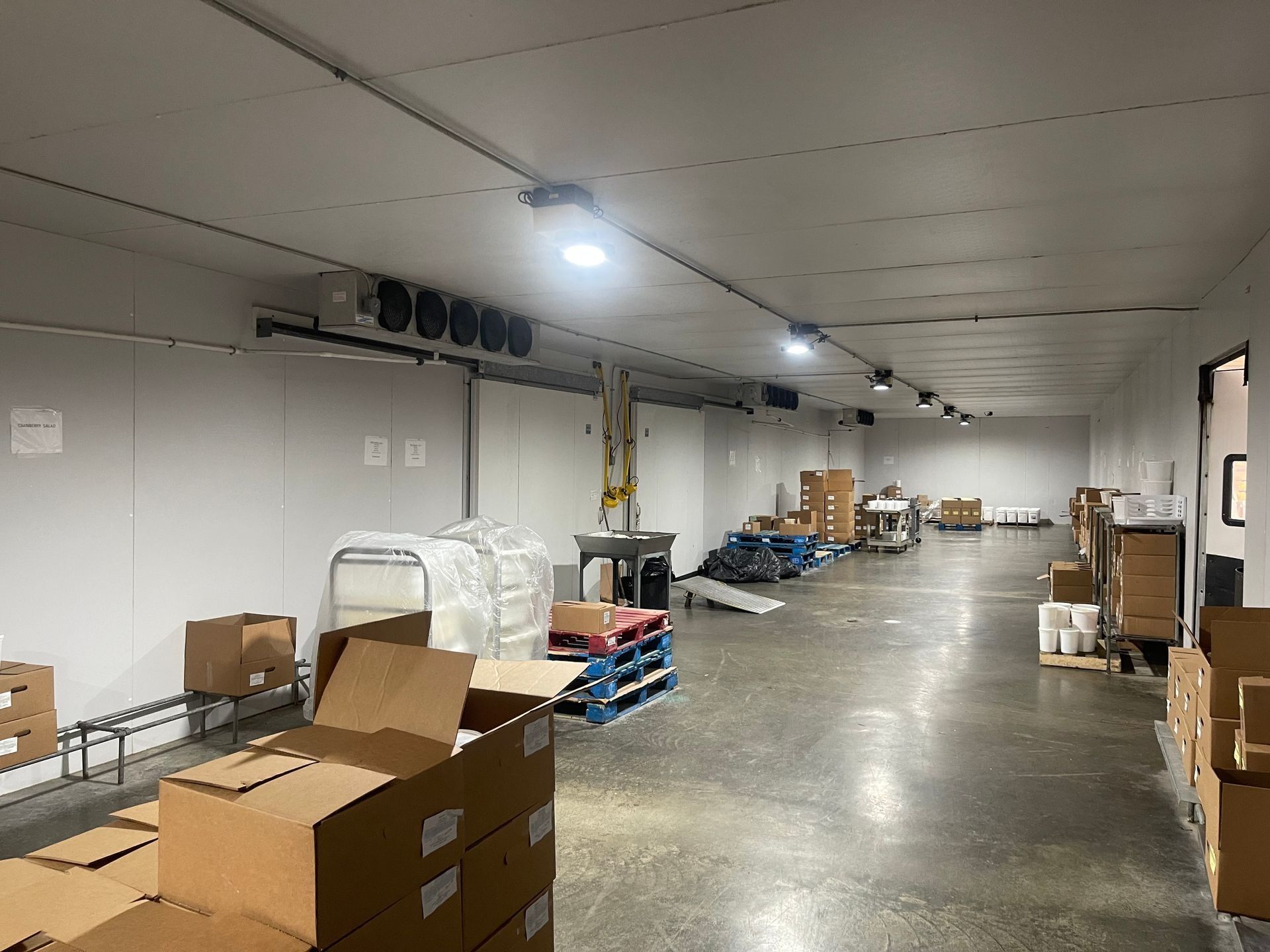 Inside a cold storage warehouse, boxes and equipment line the floor under bright lights and cooling units.