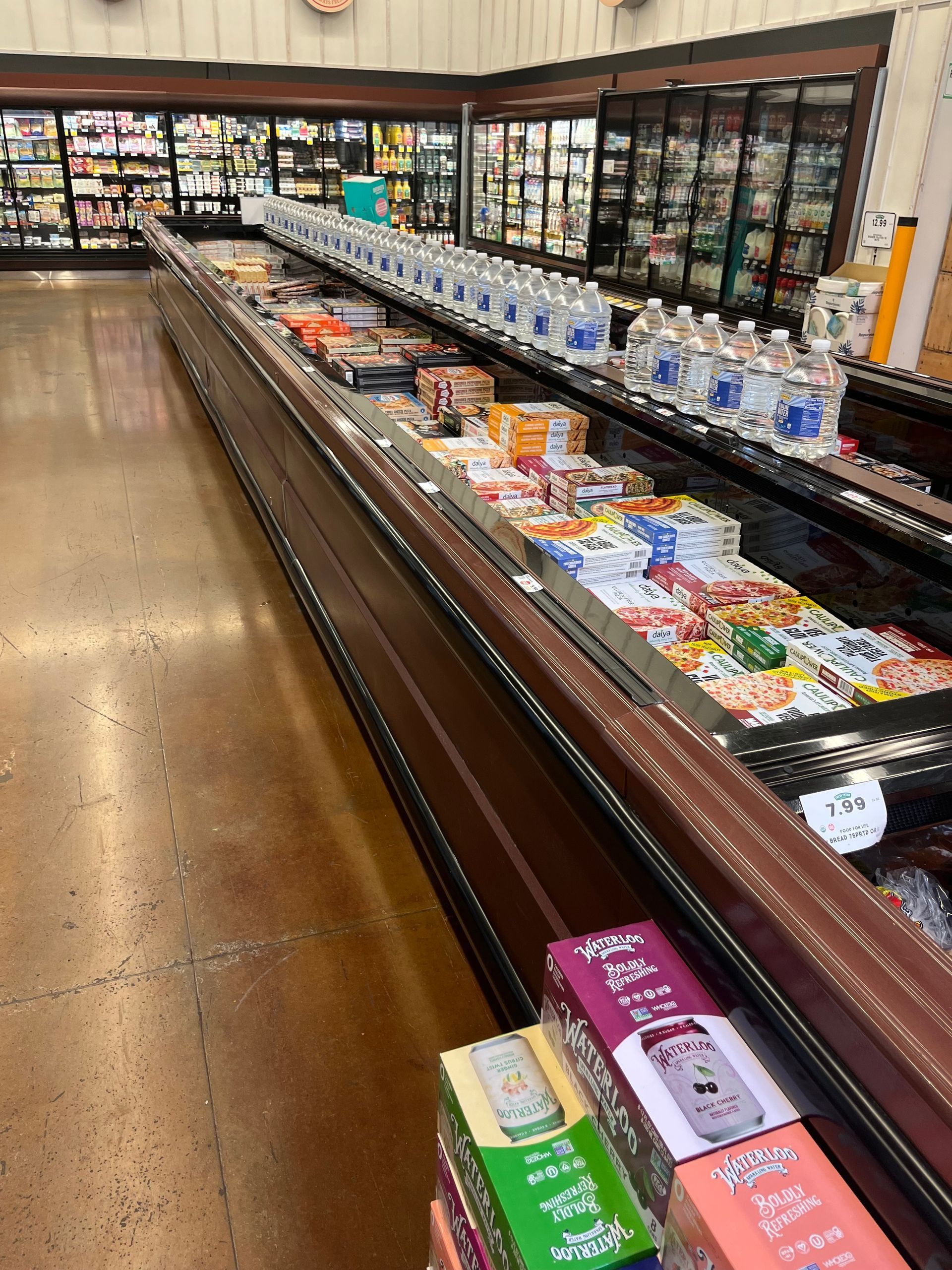 Refrigerated grocery aisle filled with frozen foods and bottled water.