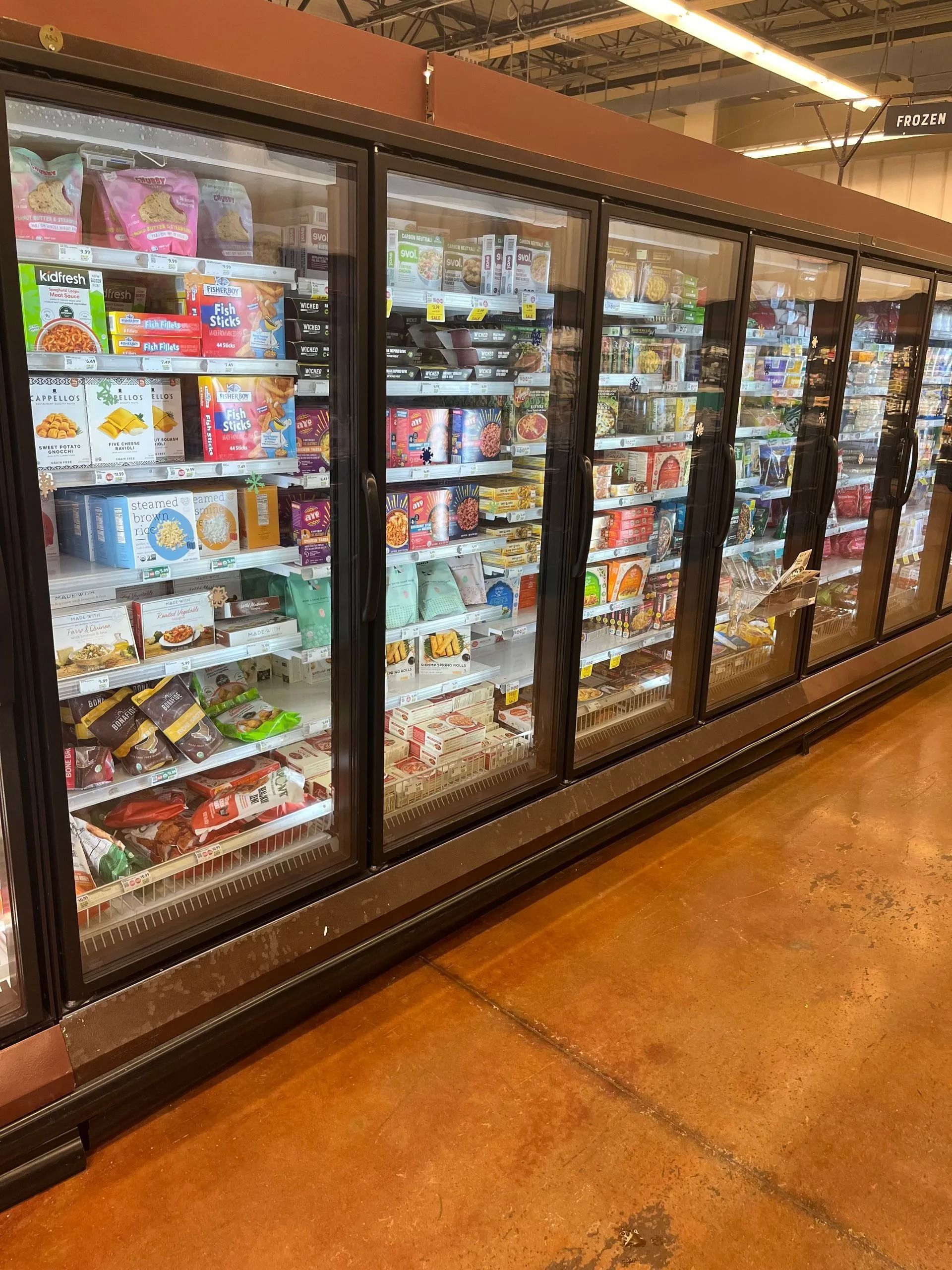 Freezer aisle in a grocery store, stocked with various frozen food items, with brown floor.