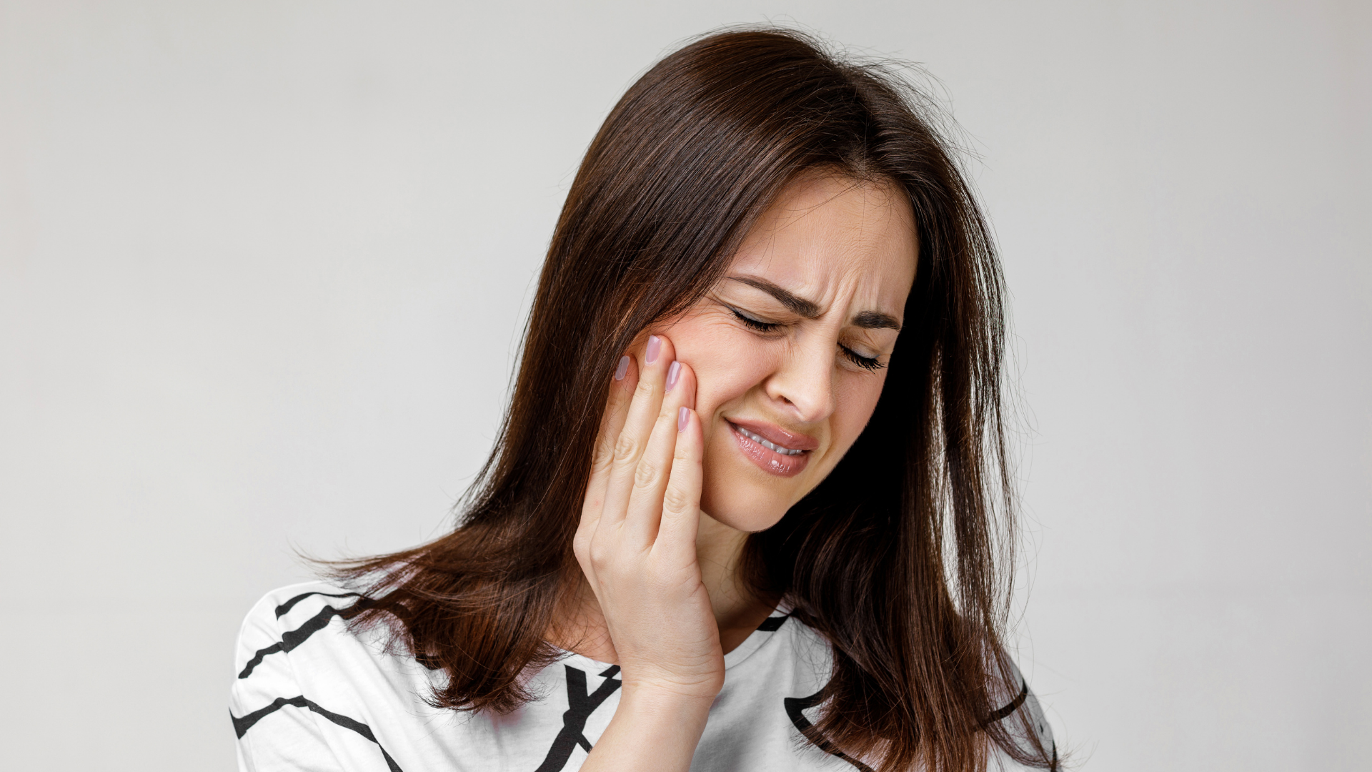 Woman grimacing and holding her cheek, suggesting tooth pain or discomfort