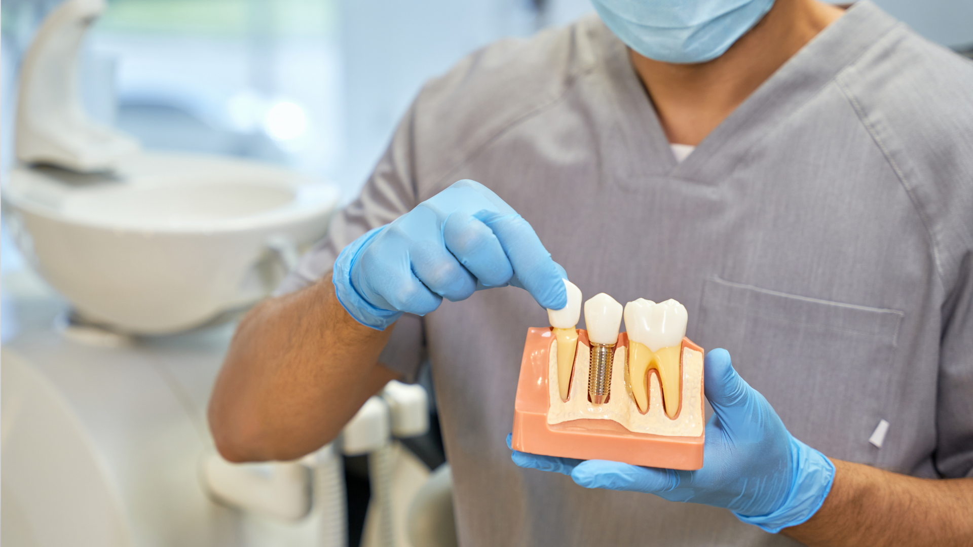 Dentist in mask and gloves pointing to a tooth model in a clinic.