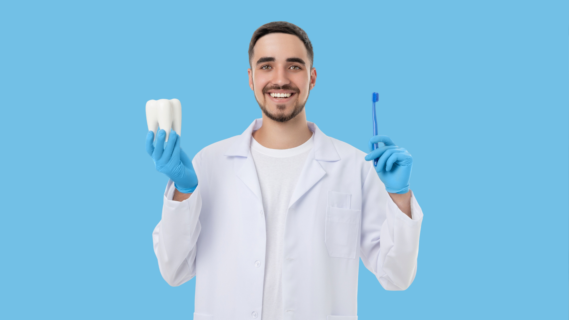 Smiling dentist in white coat holding a model tooth and toothbrush on a blue background